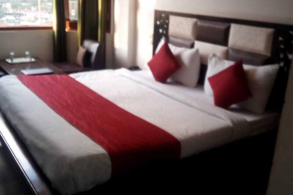 A hotel room with a large bed, a bedside table, a window with a view of the mountains, and a painting on the wall.