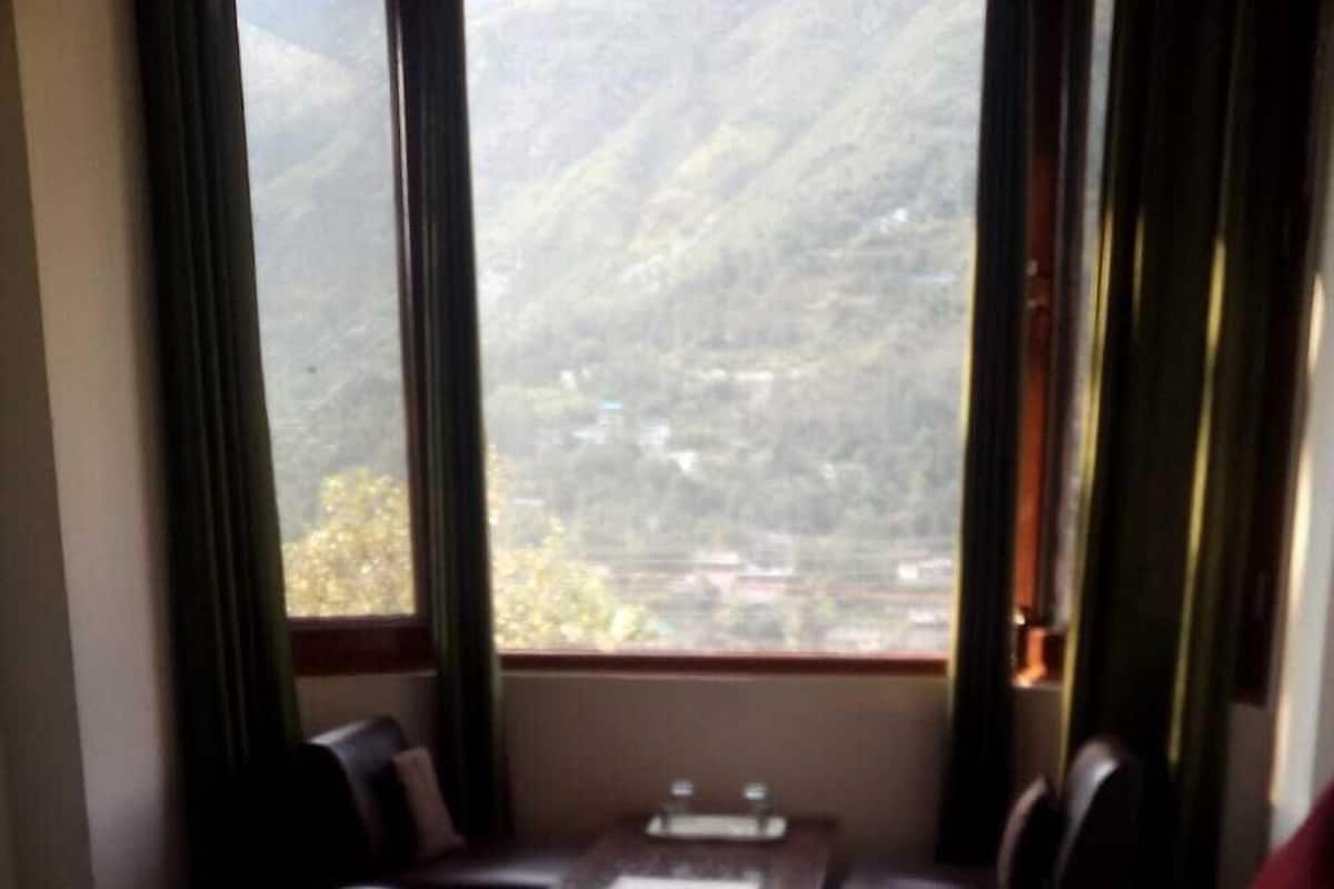 A hotel room with a bed, a small table, and a view of a mountainous landscape through the window.