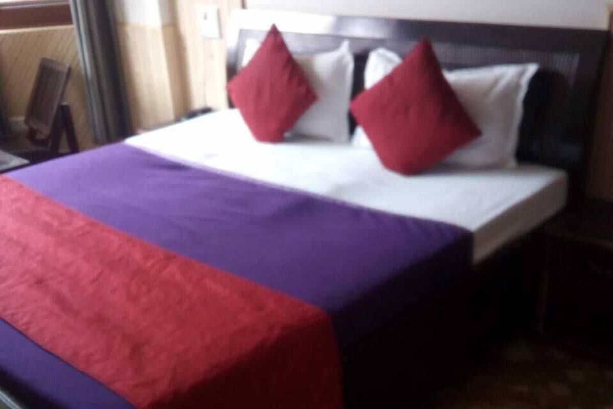 A neatly made bed with a purple and red bedspread, a white pillow, and a red pillow.