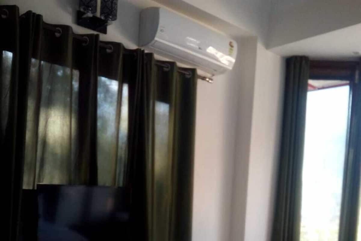 A hotel room with a bed, a TV on a stand, and an air conditioning unit.