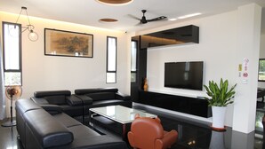 A modern living room with a black leather sofa, a glass coffee table, a flat-screen TV mounted on the wall, and a potted plant. - Morning Homestay (Puli)
