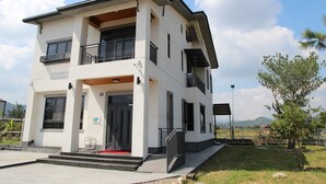 A modern two-story building with a balcony, a covered entrance, and a small outdoor seating area. - Morning Homestay (Puli)