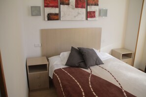 A neatly made bed with a brown blanket, two pillows, and a wooden headboard. There are two bedside tables with drawers, and a wall-mounted light fixture above the bed. - Hostal Francisco Salinas (Burgos)