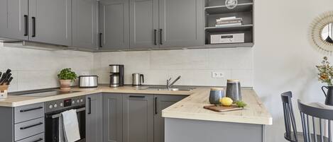Una cocina moderna con armarios grises, horno empotrado, un fregadero y una pequeña isla con tabla de cortar y fruta.