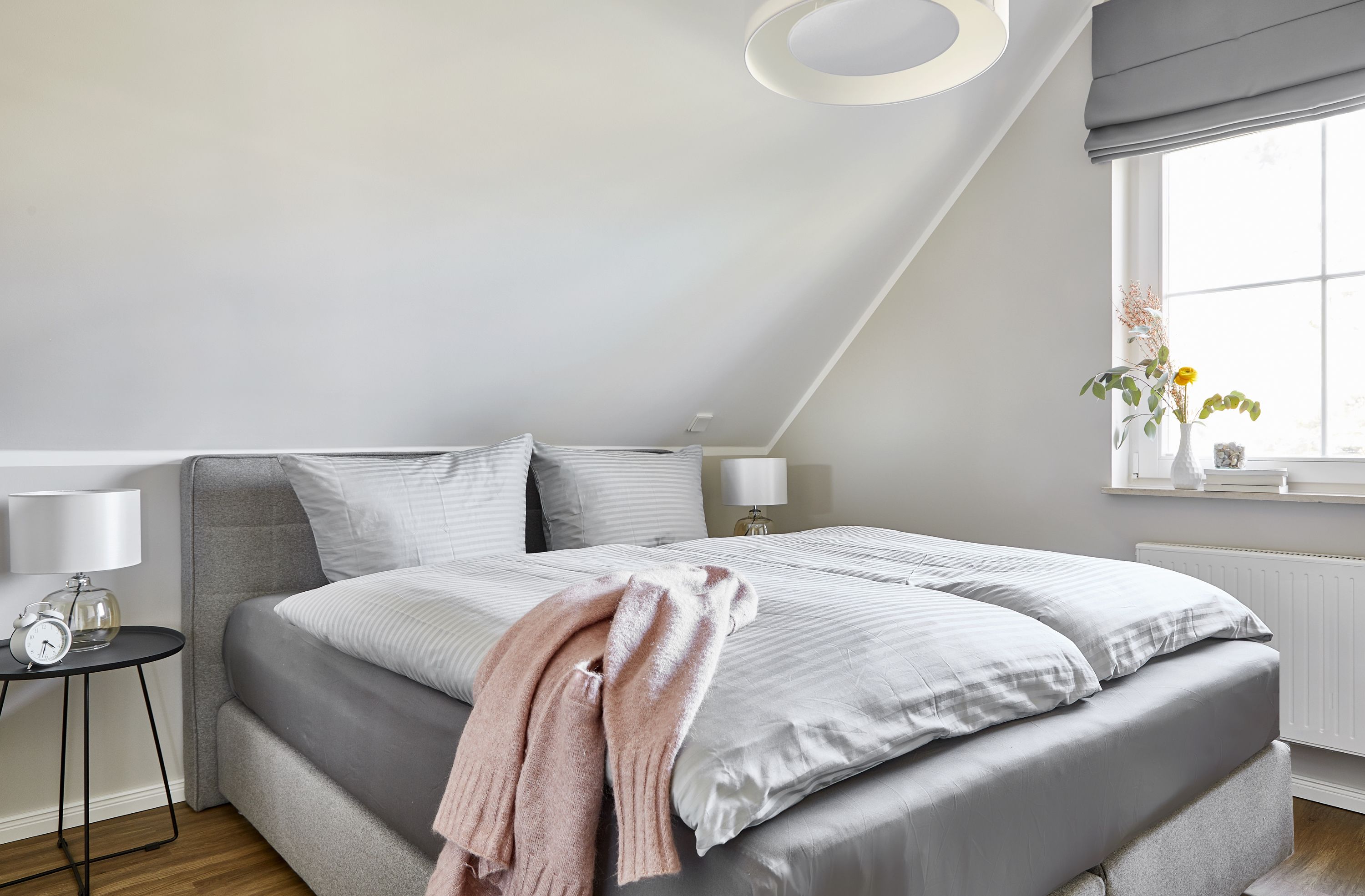 Ein Schlafzimmer mit einem großen Bett, einem Nachttisch mit Lampe, einem Fenster mit Aussicht und einer Deckenleuchte.