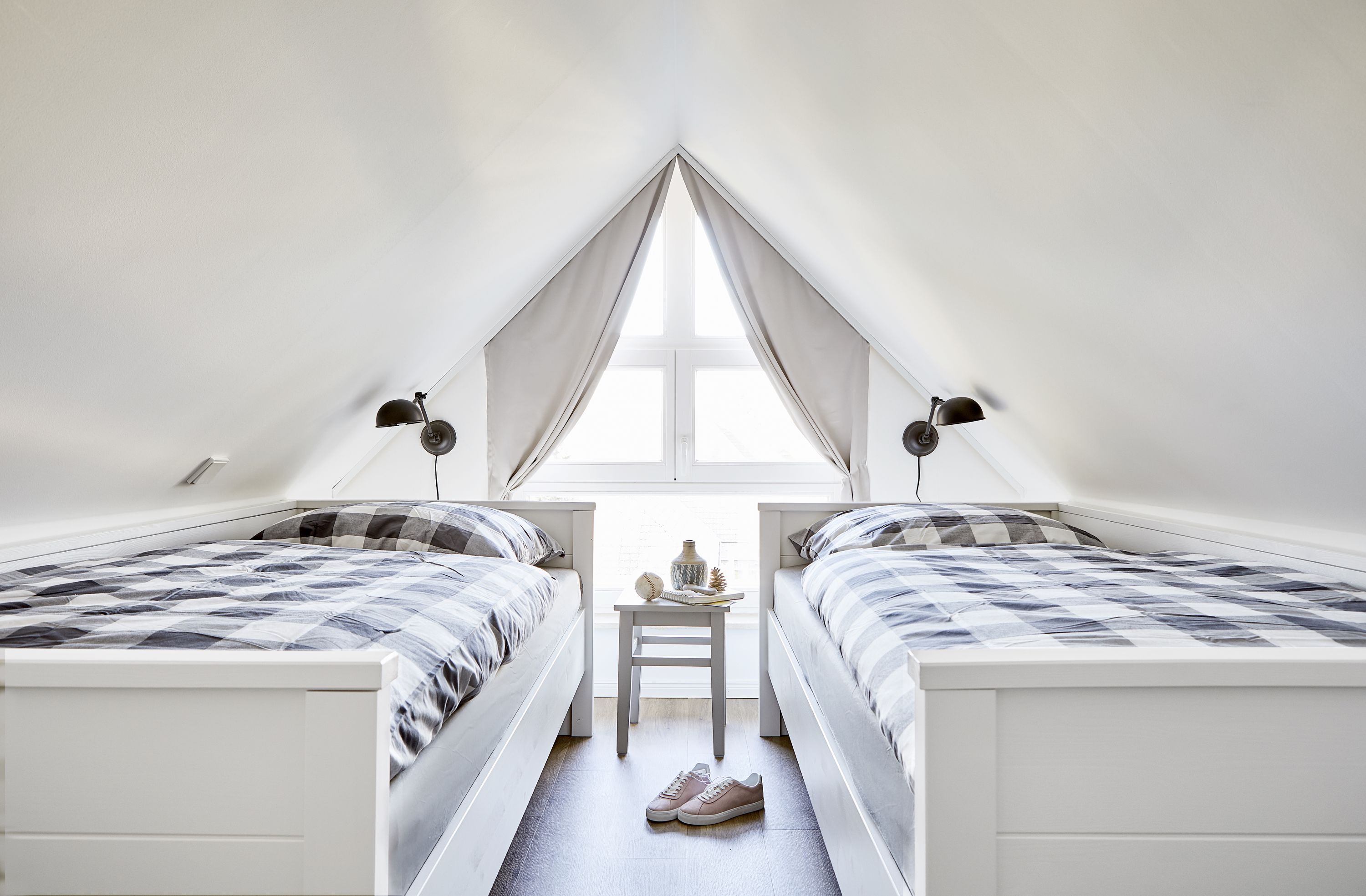 A small, triangular attic bedroom with two beds, a small table, and a window.