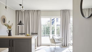 A modern kitchen with a dining area, large windows with curtains, and a view of the outdoors. - Schwedenglück Prerow (Ostseebad Prerow)