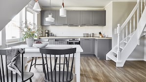 A modern kitchen with grey cabinets, a white countertop, and a dining area with a table and chairs. - Schwedenglück Prerow (Ostseebad Prerow)