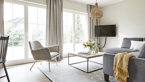 A modern living room with a grey sofa, a chair, a coffee table, and a TV mounted on the wall. - Schwedenglück Prerow (Ostseebad Prerow)