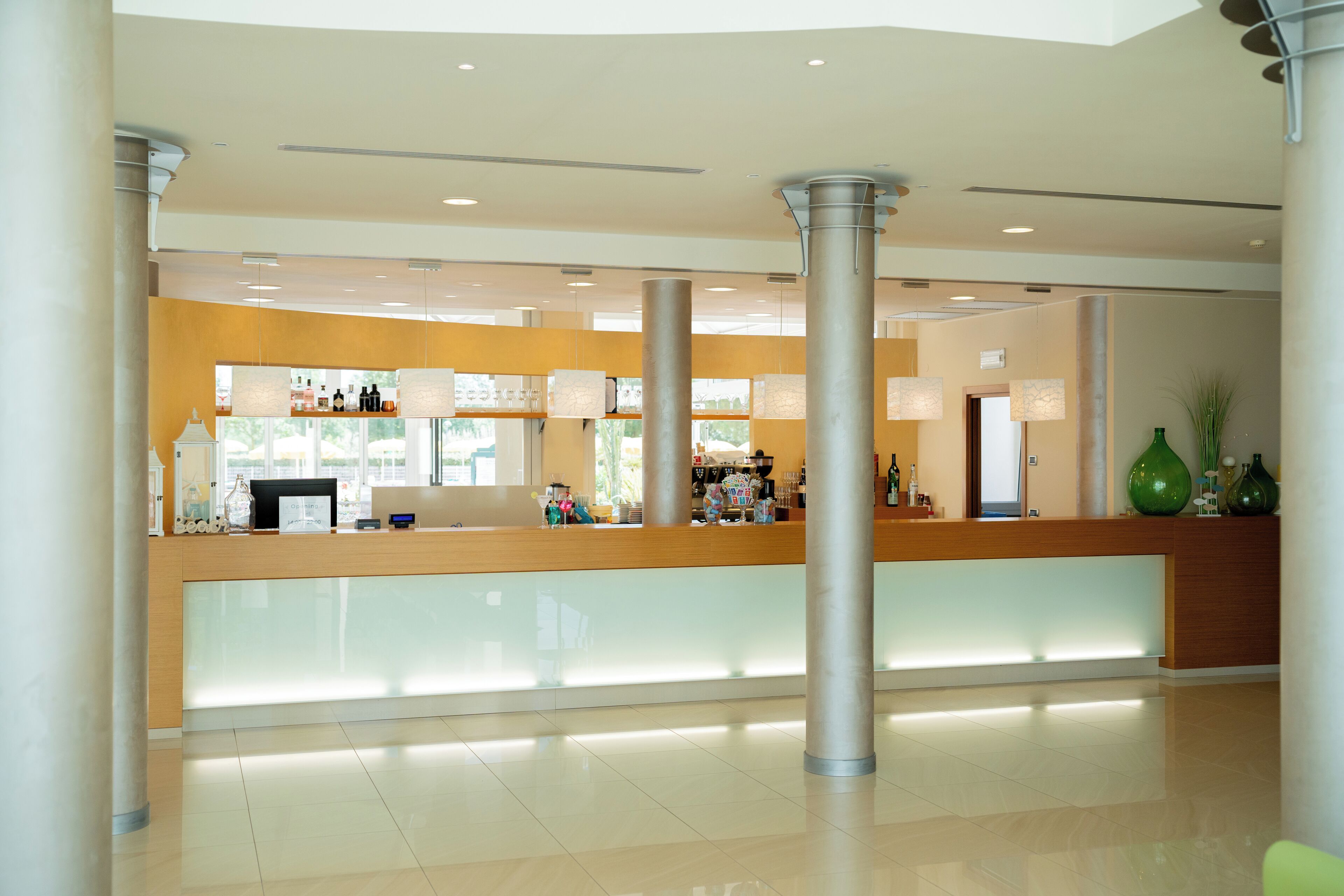 Una moderna zona de recepción con mostrador de madera, separadores de vidrio y una columna central.