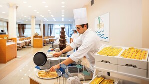 Kokki valmistaa ruokaa valoisassa, modernissa keittiössä, jossa on tarjolla buffet-tyyppinen ruokailu.
