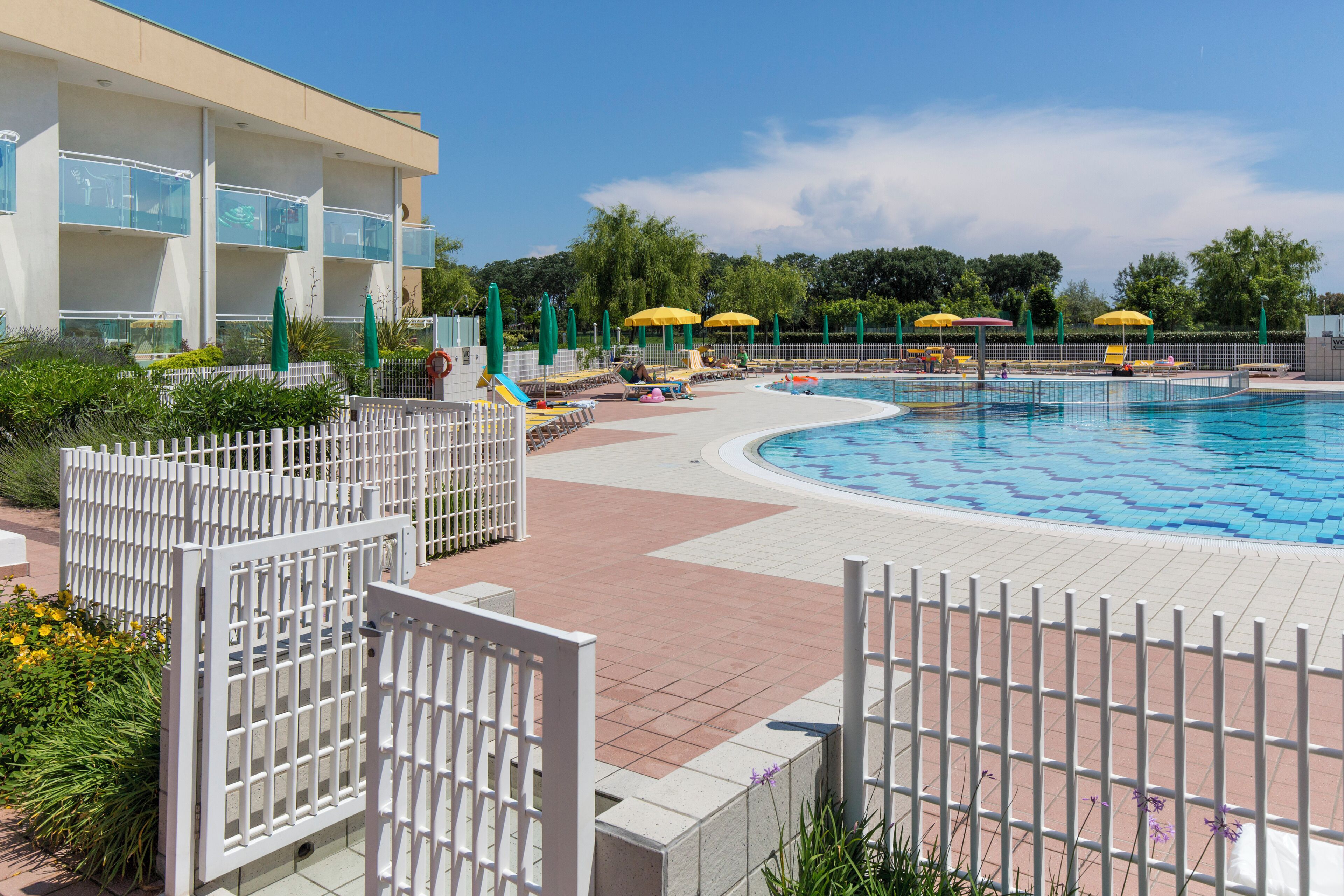 Uma área de piscina com cerca branca, guarda-sóis amarelos e espreguiçadeiras.