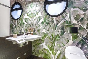 A bathroom with a large mirror, a sink, and a toilet. The wall features a leafy pattern. - COSTA RICA BIBIONE Spa (San Michele al Tagliamento)