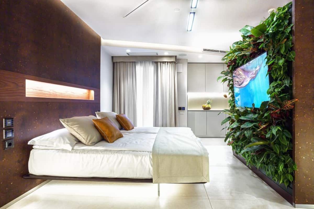 Une chambre moderne avec un grand lit, un banc, un téléviseur fixé au mur et un jardin vertical.