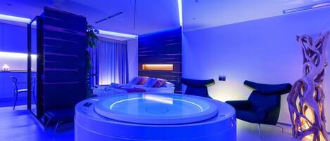 Quarto moderno com área de estar circular, sofá com almofadas e uma escultura de madeira.