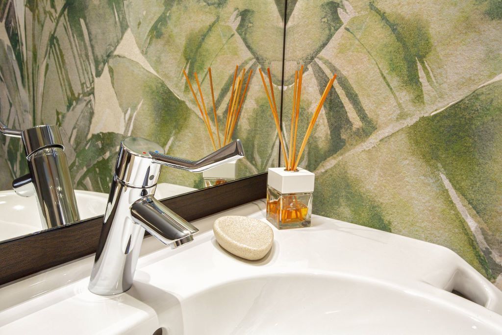A bathroom sink with a chrome faucet, a soap dish, and a reed diffuser.