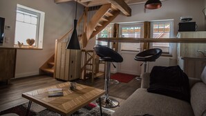 A modern living room with a wooden staircase, a black bar stool, a sofa, and a dining table. - Ferienhaus am Eichenhof Zum Speicher (Walsrode)