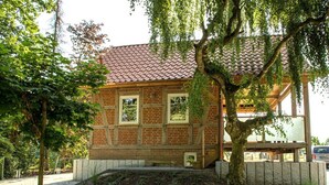 A brick building with a tiled roof, a staircase leading to a covered area, and a tree in the foreground. - Ferienhaus am Eichenhof Zum Speicher (Walsrode)