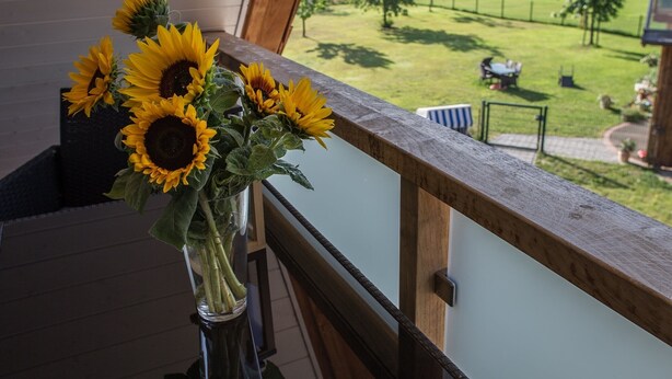 A balcony with a wooden railing and a vase of sunflowers on a reflective surface. - Ferienhaus am Eichenhof Zum Speicher (Walsrode)