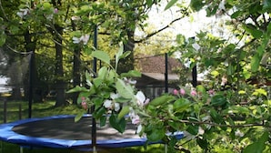 A trampoline surrounded by lush greenery and flowering trees. - Ferienhaus am Eichenhof Zum Speicher (Walsrode)