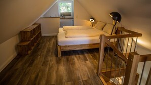 A bedroom with a sloped ceiling, a bed, a nightstand, a lamp, and a wooden staircase. - Ferienhaus am Eichenhof Zum Speicher (Walsrode)