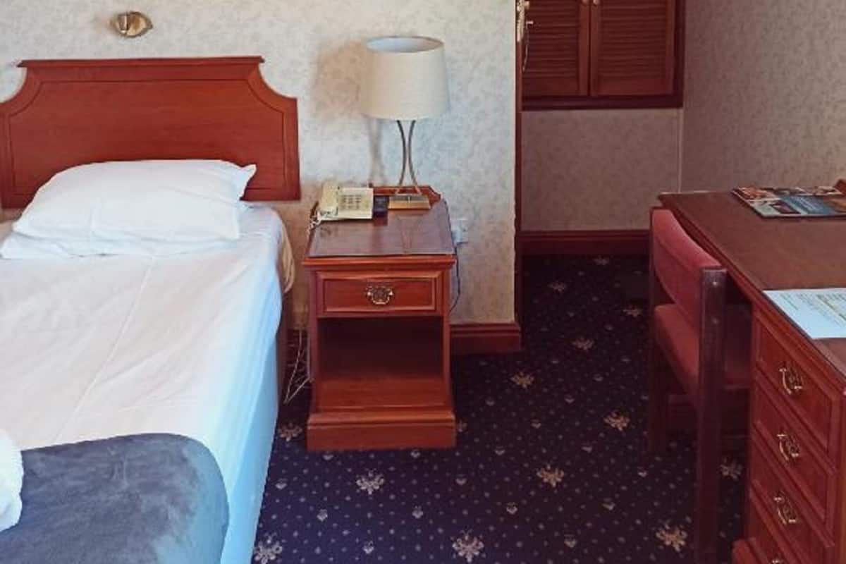 A hotel room with a bed, bedside table with a lamp, a desk, and a wardrobe.