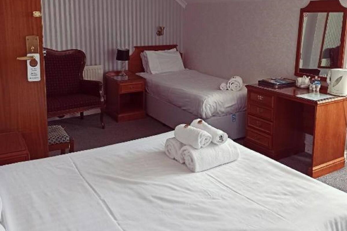 A hotel room with two beds, a desk, a chair, a nightstand, and a mirror.