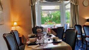 A dining room with a table set for four, chairs, a window with curtains, and a clock on the wall. - Crystal Hotel (Cambridge)