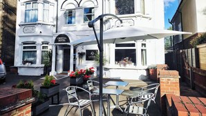 A white building with a sign reading "Crystal Hotel" and "Savour." There are outdoor tables and chairs, and flower planters. - Crystal Hotel (Cambridge)