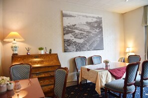 A dining area with a table, chairs, a wooden chest of drawers, and a wall-mounted painting. - Crystal Hotel (Cambridge)