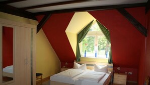 A bedroom with a sloped ceiling, a bed with white bedding, a wardrobe, and a window with green curtains. - Ferienwohnung Zum Storchenblick (Walsrode)