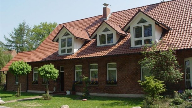 A two-story brick house with a red-tiled roof, dormer windows, and a chimney. - Ferienwohnung Zum Storchenblick (Walsrode)