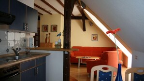 A kitchen with a central island, a dining area with a red sofa, and a view of the living room. - Ferienwohnung Zum Storchenblick (Walsrode)