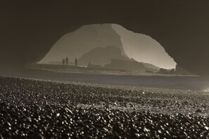 A beach with a large rock formation in the background and people walking on the shore. - Tifawin Home & Garden (Mirleft)