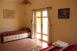 A bedroom with a bed, a window with curtains, a wall-mounted picture, and a patterned rug. - Tifawin Home & Garden (Mirleft)