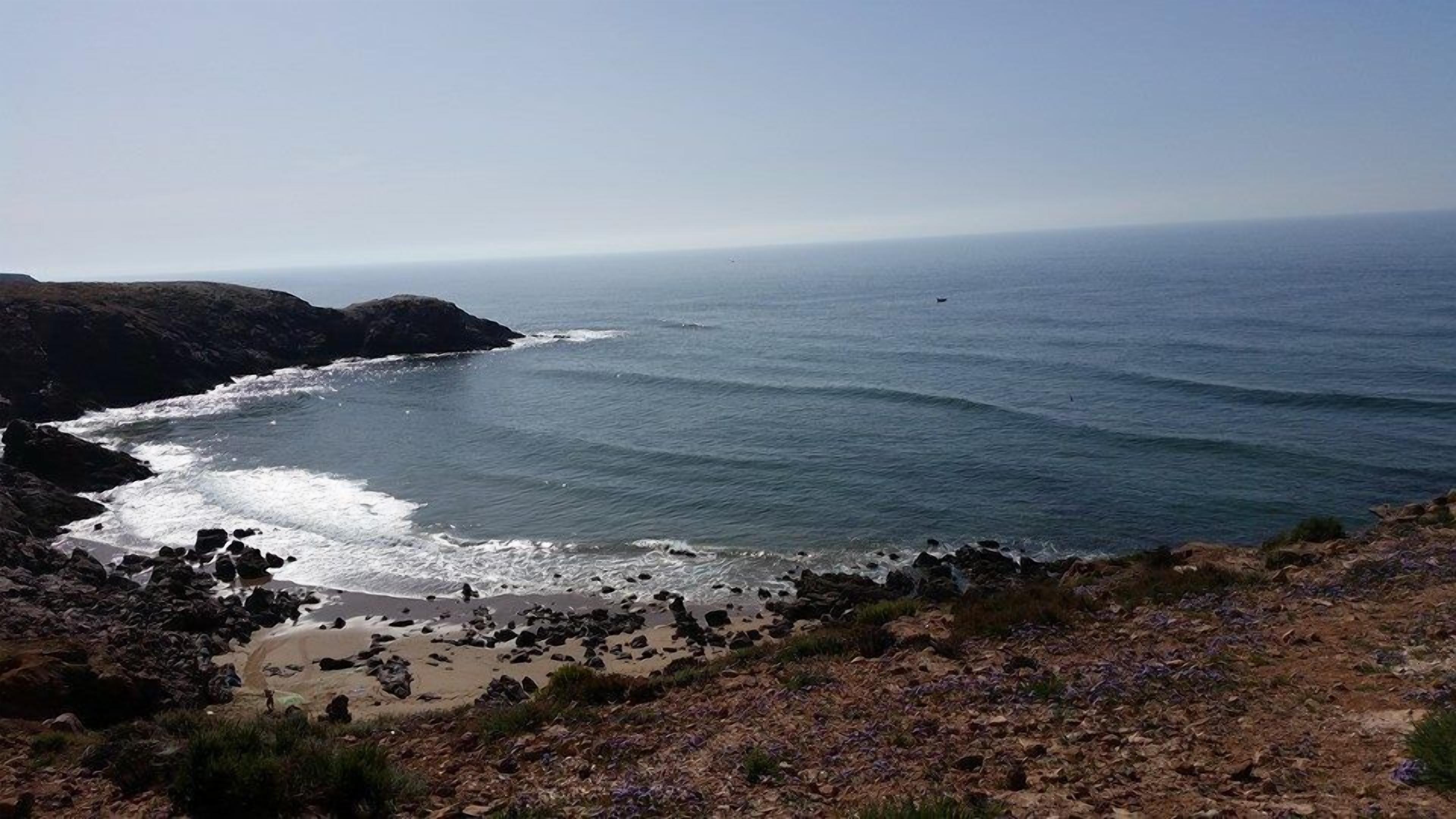 A coastal landscape with rocky terrain, a sandy beach, and the ocean.