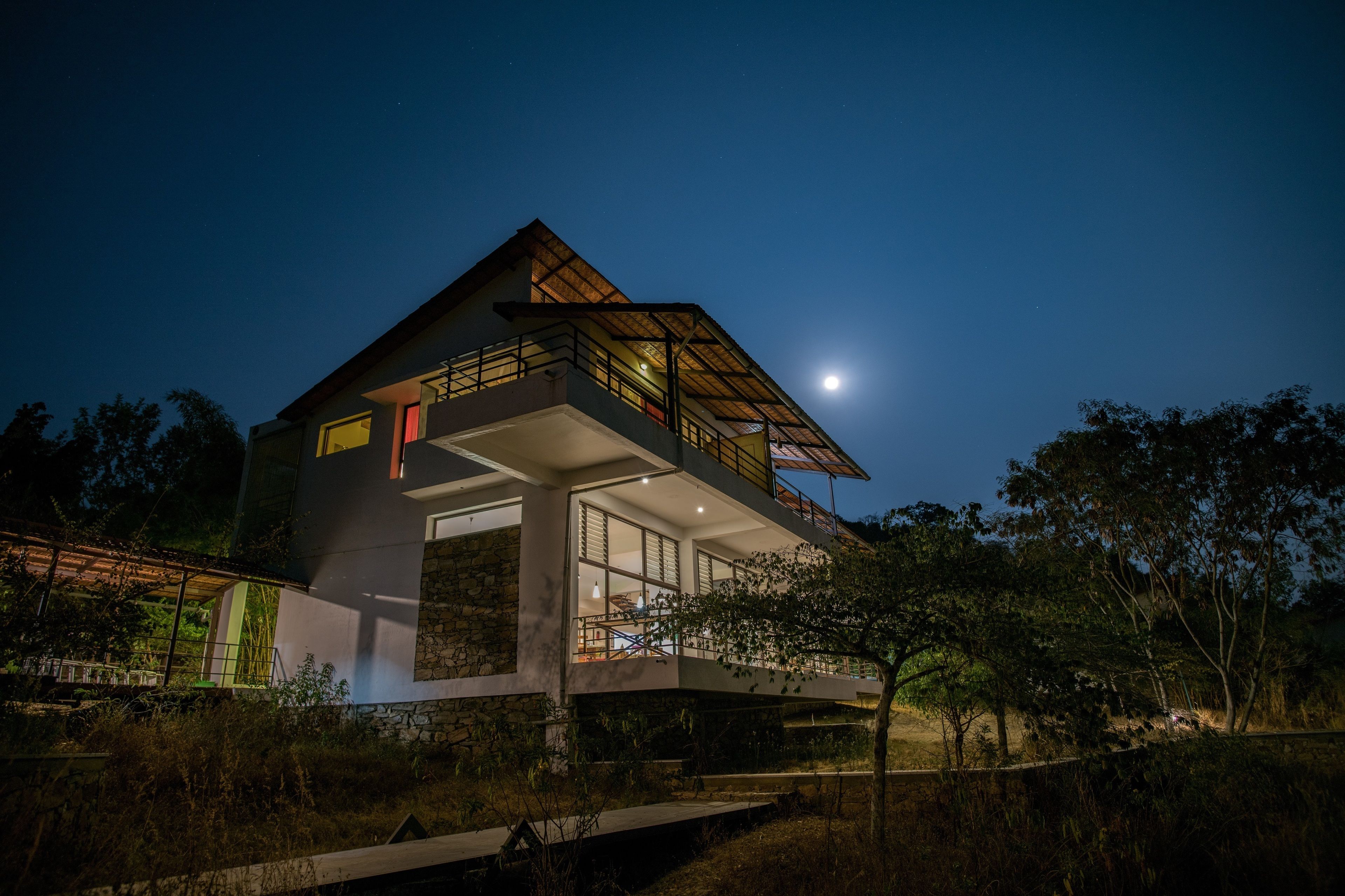 Una casa moderna con un ampio balcone, una base in pietra e vista sul cielo notturno.