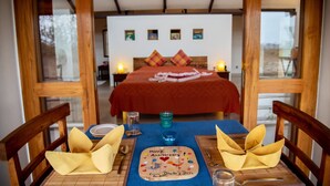 Een eettafel gedekt voor twee personen, met een rode sprei en kussens op de achtergrond.