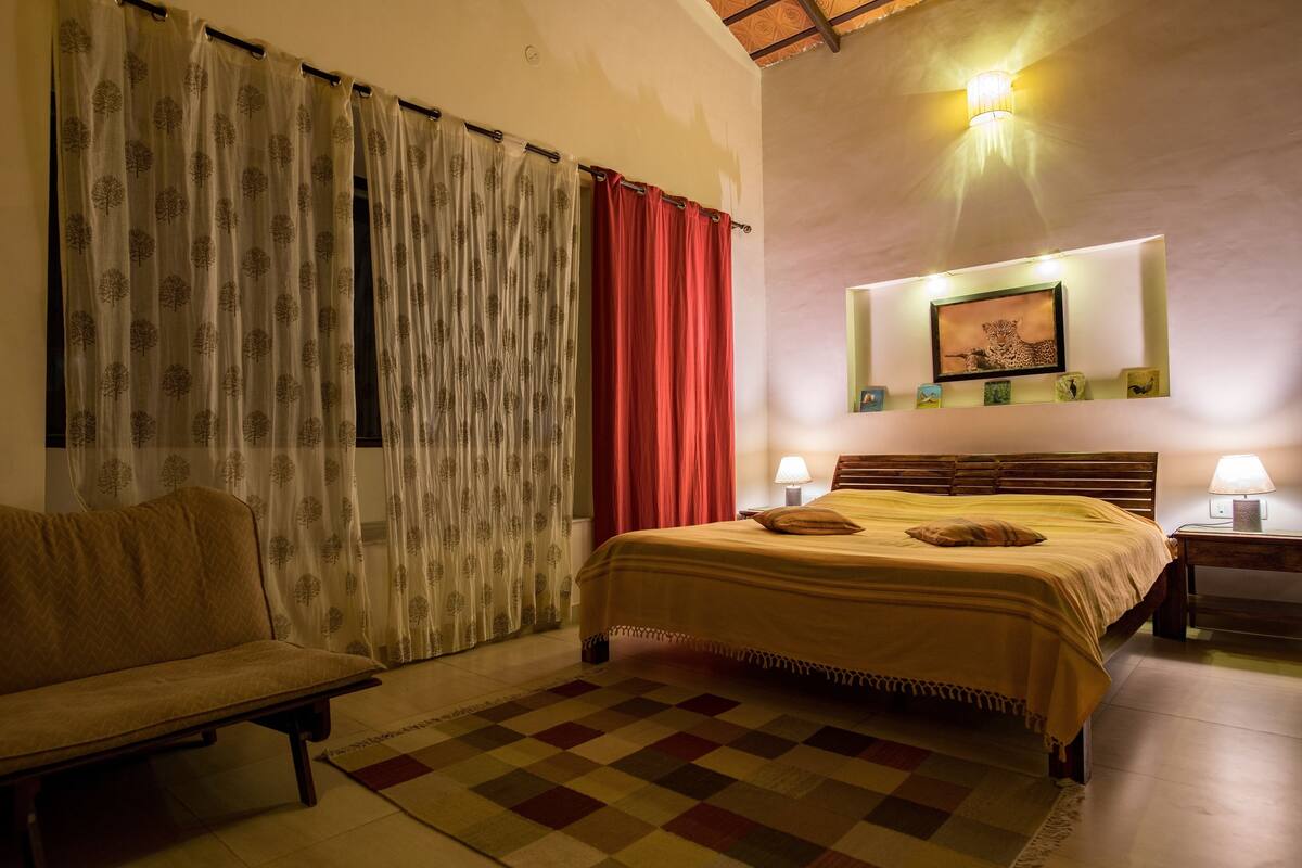 Une chambre à coucher comprenant un lit, un canapé, un tapis à carreaux, une table de chevet, une lampe et un tableau accroché au mur.