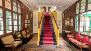 A grand staircase with a red carpet, flanked by wooden railings and potted plants. - Windamere Hotel (Darjeeling)