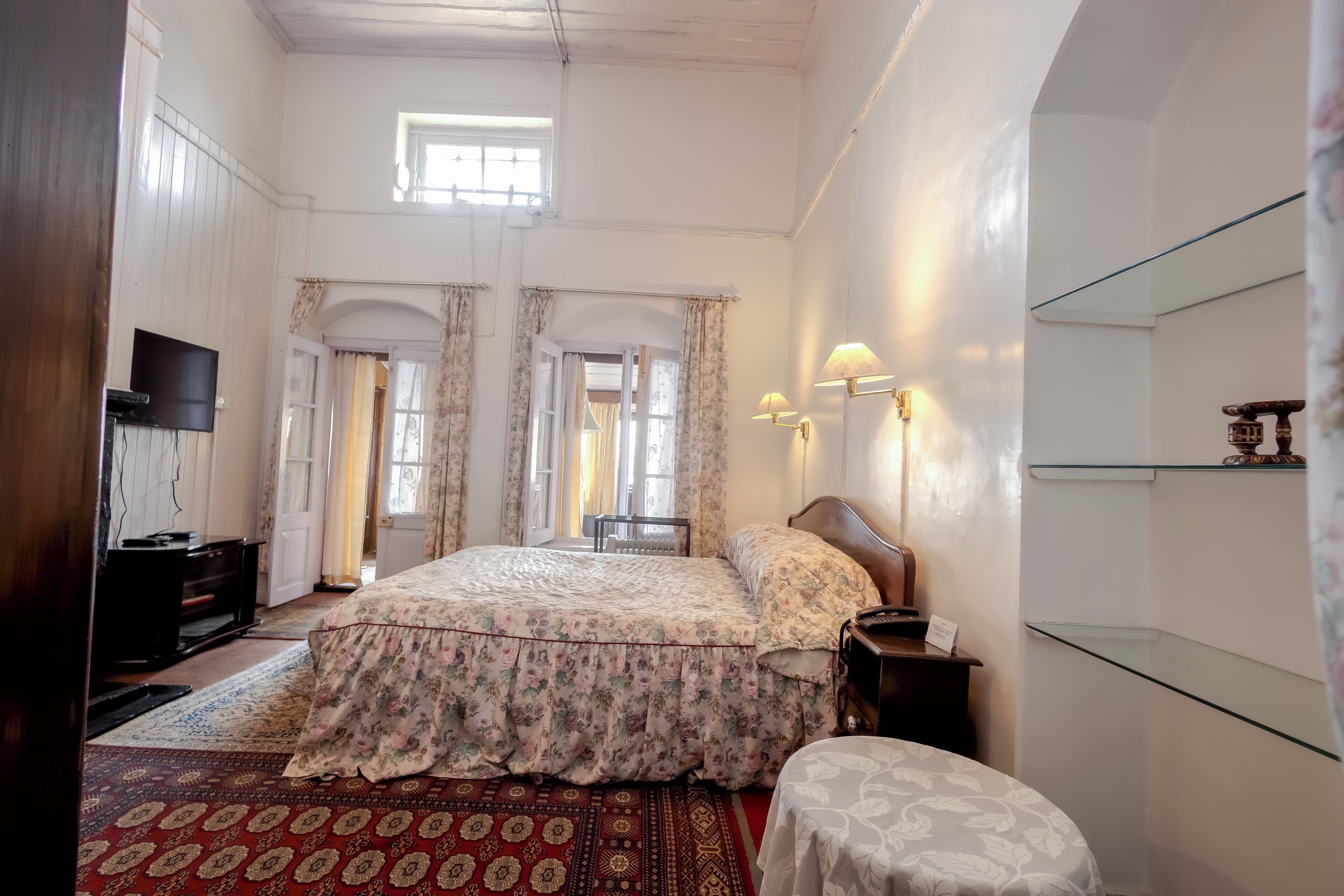 Un dormitorio con una cama grande, televisor, escritorio y repisa de vidrio.