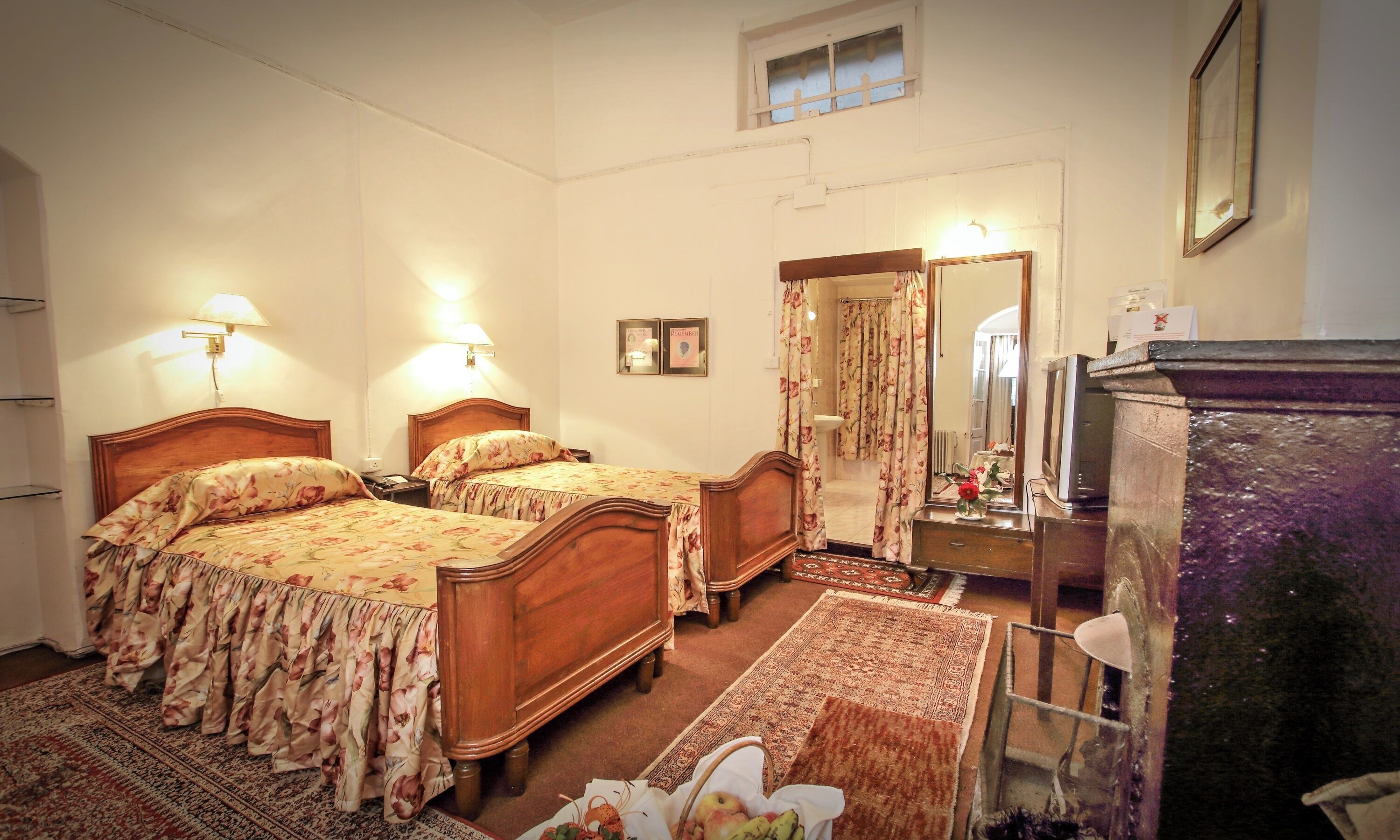 A bedroom with two wooden beds, a dresser, a mirror, and a small table with a vase.
