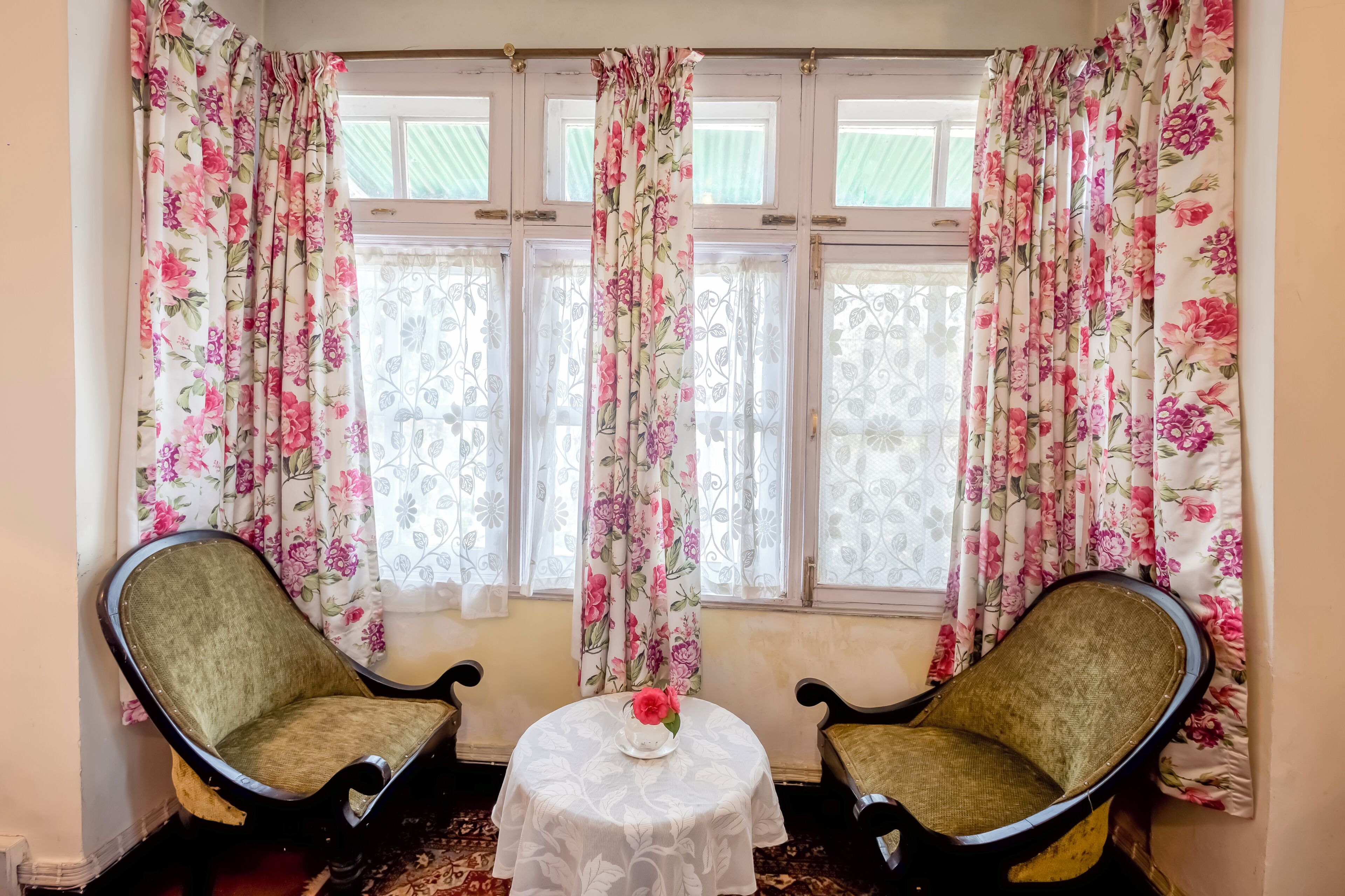 Een kamer met twee fauteuils, een tafeltje met een vaas en bloemen gordijnen.