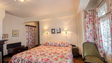 Un dormitorio con colcha estampada de flores, una silla, un escritorio y un aparador.