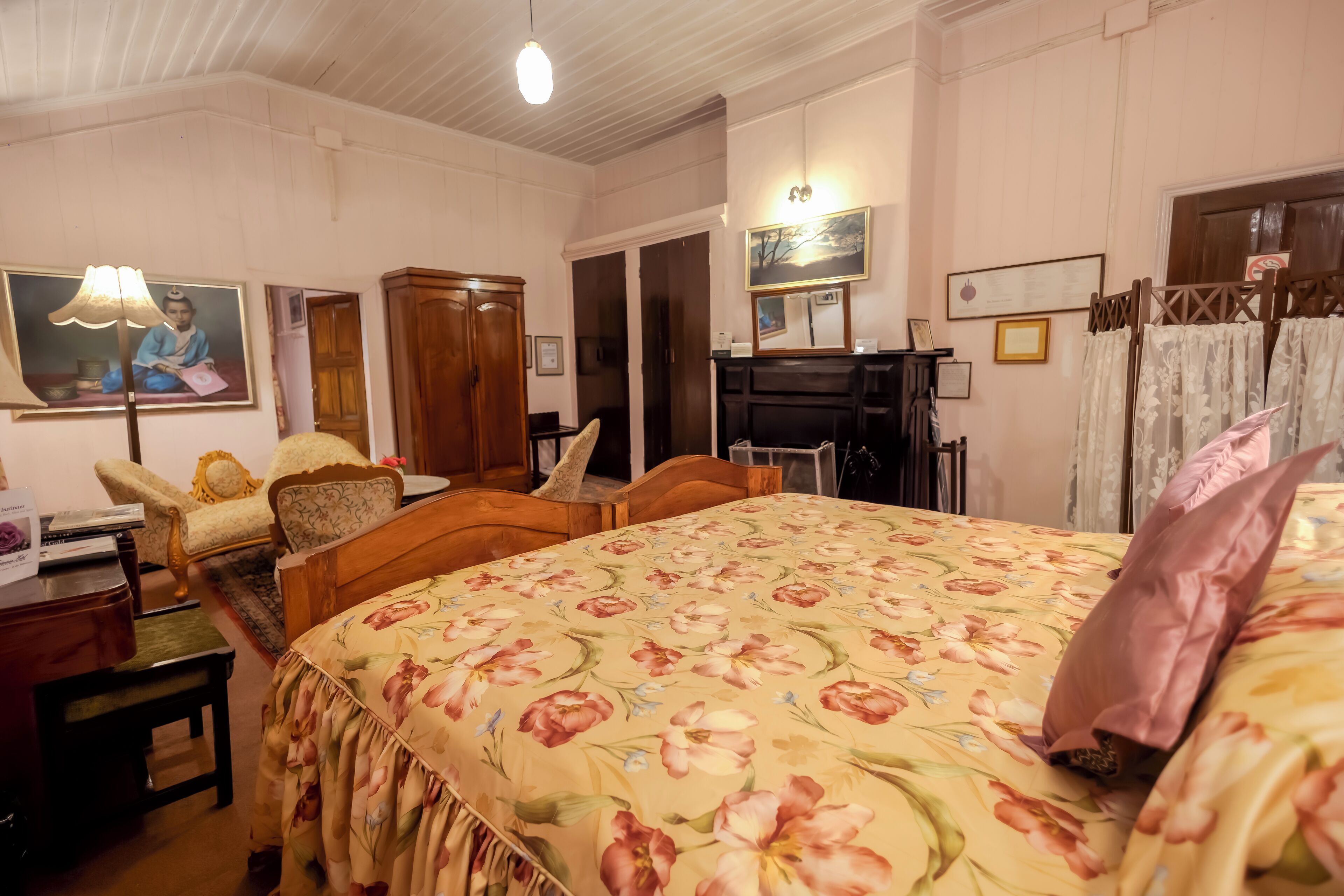 Una habitación con una colcha estampada con motivos florales, muebles de madera, un escritorio con lámpara y un cuadro en la pared.