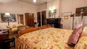 Una habitación con una colcha estampada con motivos florales, muebles de madera, un escritorio con lámpara y un cuadro en la pared.