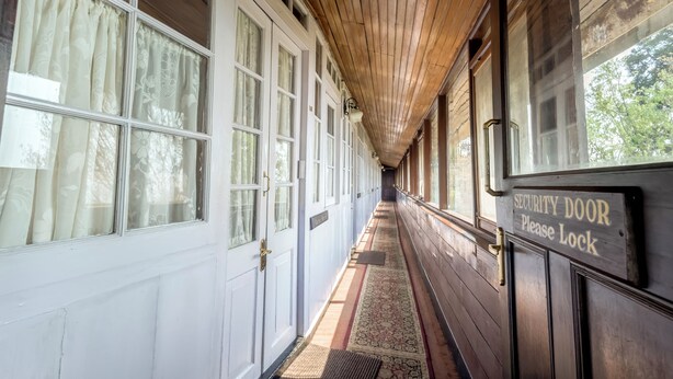 A corridor with wooden paneling, large windows with curtains, and a security door sign. - Windamere Hotel (Darjeeling)