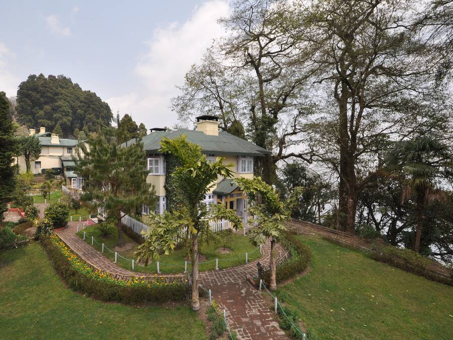 Una casa con techo verde, rodeada por un jardín con un sendero y una valla.