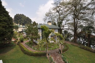 A house with a green roof, surrounded by a garden with a pathway and a fence.