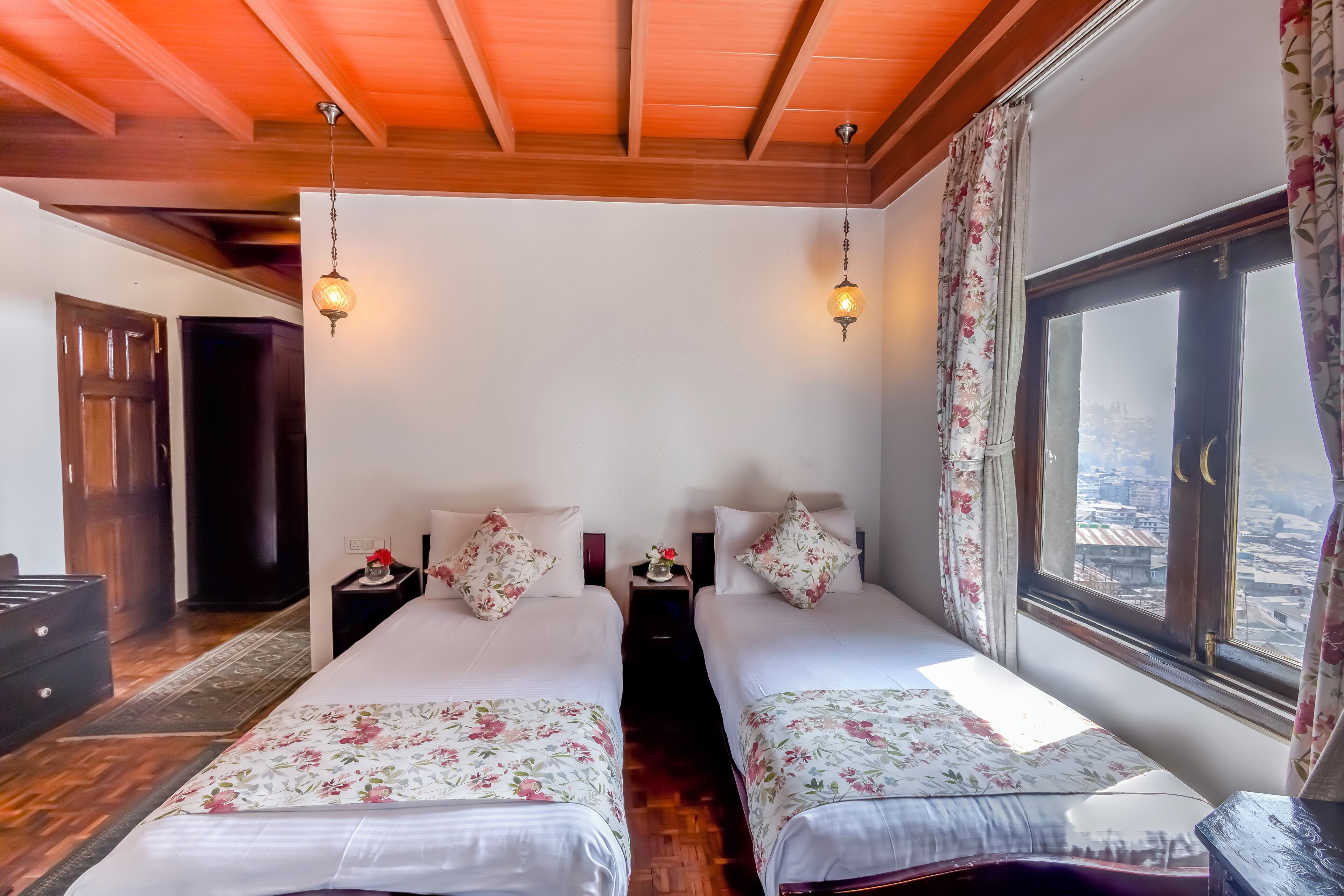 Una habitación con dos camas, vigas de madera en el techo, un ventanal con vistas y una mesita de noche con lámpara.
